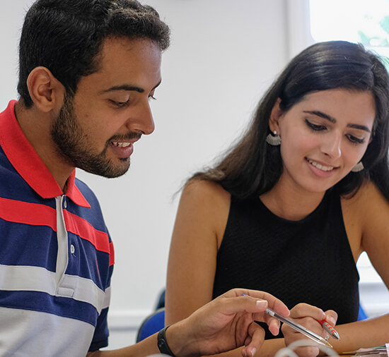 Male and female students smiling as they look at a course book in class